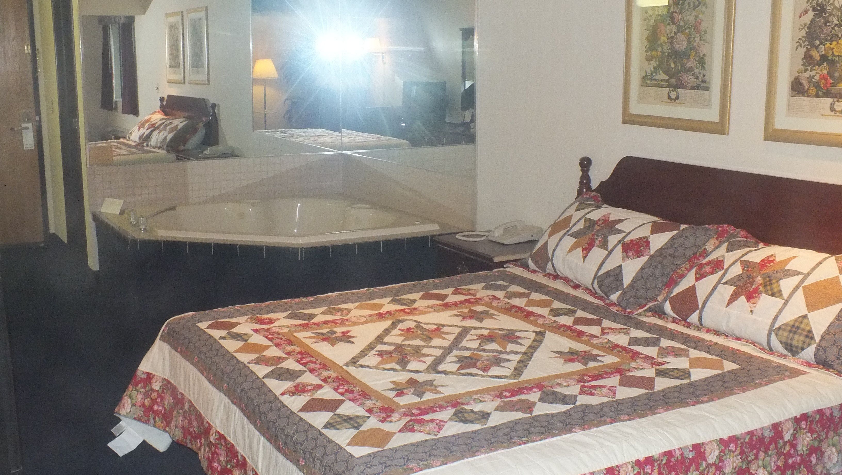 A hotel room with a large bed, a bathtub, and a mirror reflecting the room.