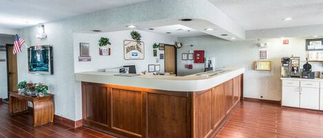 Un área de recepción con un mostrador de madera, un cartel de lobby con la palabra 'registro' y una máquina de café.