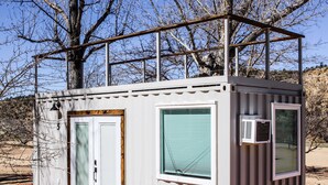A small, single-story building with a metal roof, a door, and a window. - Cliffside Tiny Home Container  #5 (Orderville)
