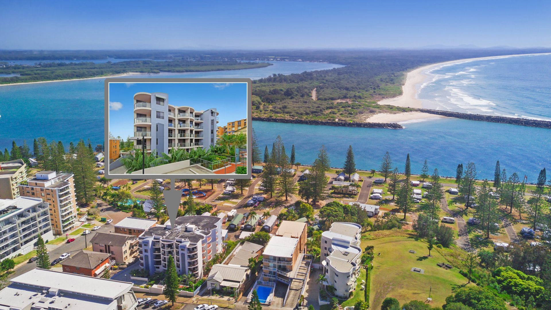 A coastal residential area with a view of the ocean, a small beach, and a large building with multiple balconies.
