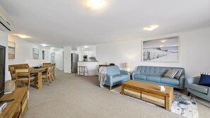 Een moderne woonkamer met een blauwe bank, een houten salontafel en een eethoek met een houten tafel en stoelen.