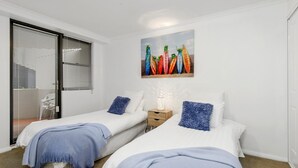 Une chambre avec deux lits simples, une table de chevet avec une lampe et un tableau au mur.