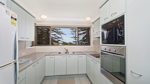 A kitchen with a window, stainless steel appliances, and light-colored cabinets.