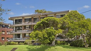 A multi-story residential building with balconies, a well-maintained lawn, and a sign indicating the address. - Quarterdeck 7, 7 Stewart Street (Port Macquarie)