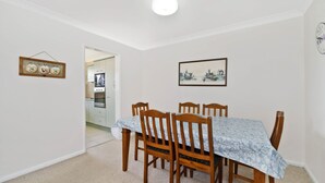 A dining area with a table and chairs, a kitchen in the background, and a wall with a framed picture. - Quarterdeck 7, 7 Stewart Street (Port Macquarie)