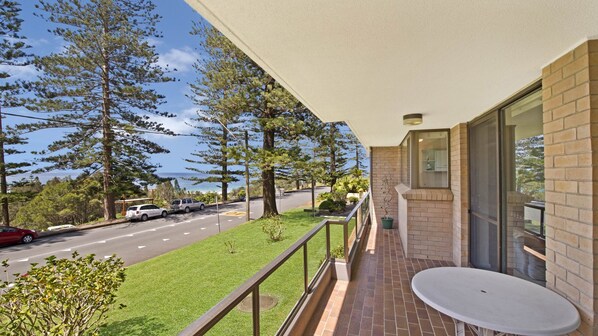 A balcony with a view of a road and trees, a table, and a potted plant.