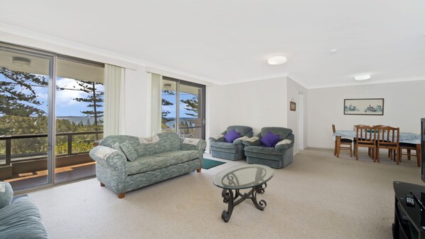 A spacious living area with a sofa, two armchairs, a glass coffee table, and a dining table with chairs.