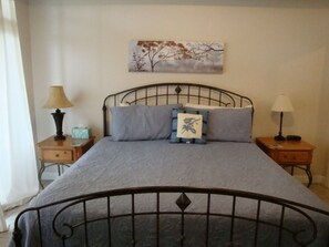 A bedroom with a metal bed frame, a grey bedspread, two bedside tables with lamps, and a wall-mounted painting.