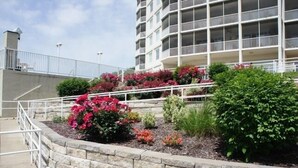 Ein mehrstöckiges Hotel mit einer Steinsichtmauer und einem angelegten Garten mit verschiedenen Sträuchern und Blumen.
