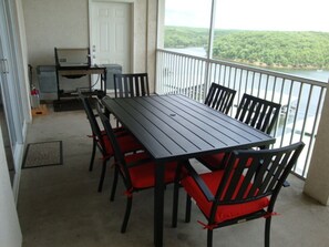 A balcony with a table and chairs, a door, and a view of a forest and water.