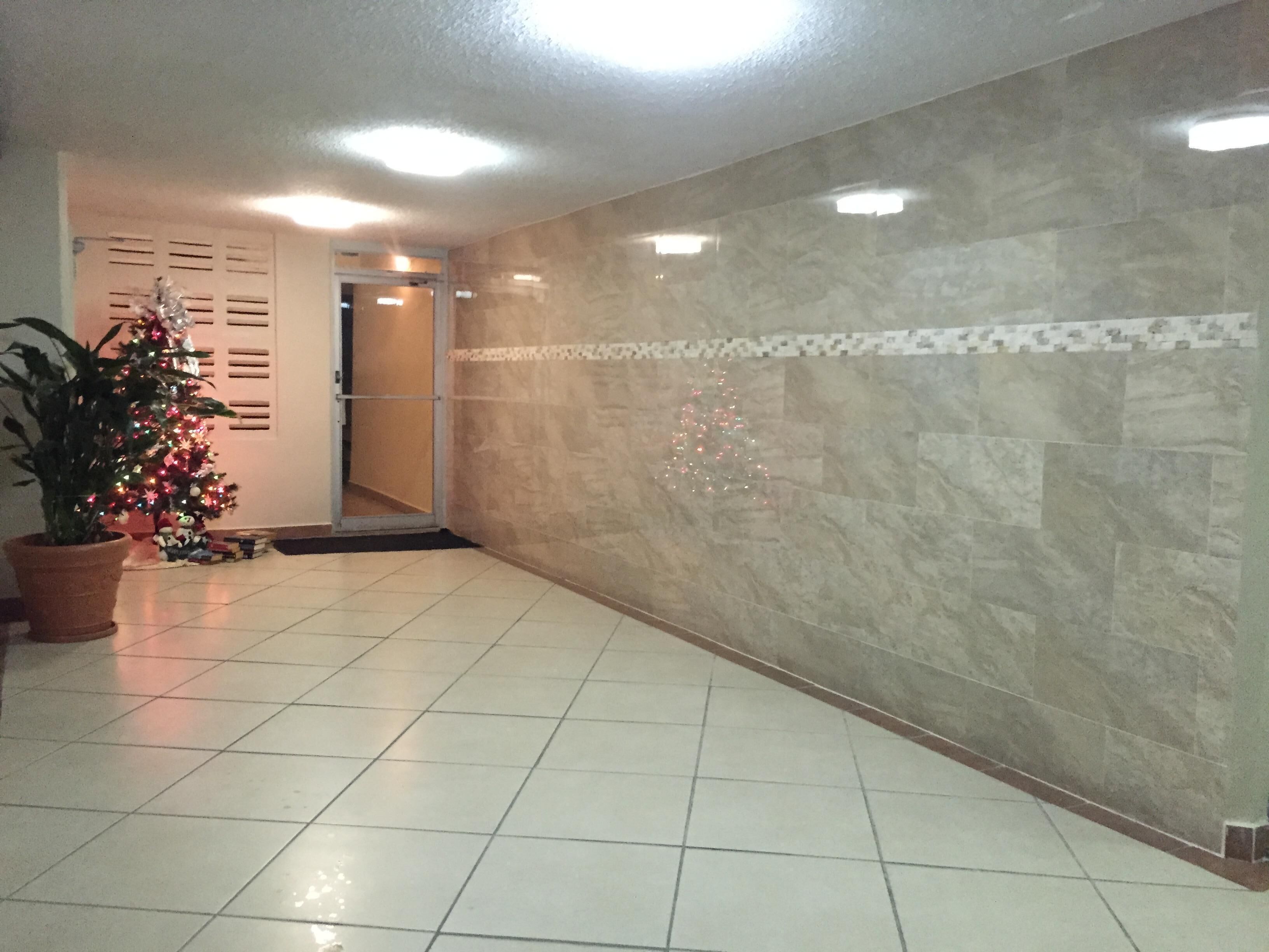 Ein Korridor mit Fliesenboden, einem Blumentopf, einem Weihnachtsbaum und einer Tür zu einem anderen Raum.