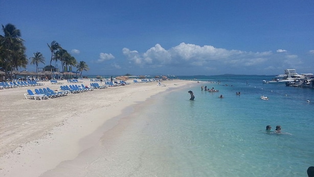 Ein Strand mit klarem türkisblauem Wasser, weißem Sand und blauen Liegestühlen.