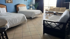 Ein Hotelzimmer mit zwei Betten, einem Schlafsofa, einem kleinen Tisch und einer Topfpflanze.