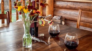 A wooden cabin interior with a dining table, a vase of flowers, two wine glasses, and a bottle. - Corkins Lodge (Chama)