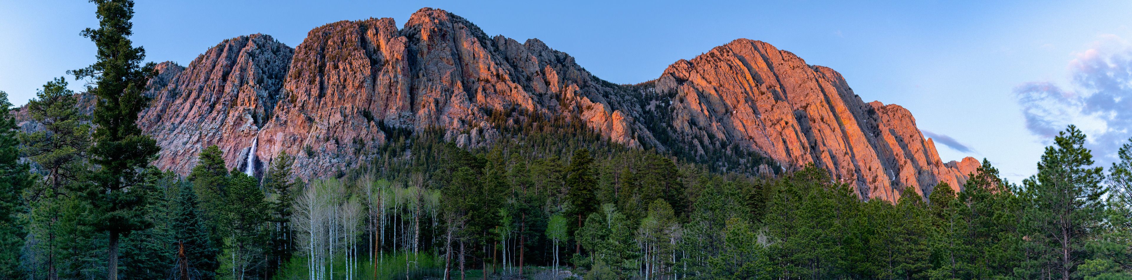 A mountain with a waterfall at its base, surrounded by dense forest.