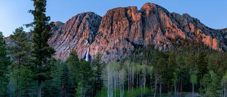 A mountain with a waterfall at its base, surrounded by dense forest.