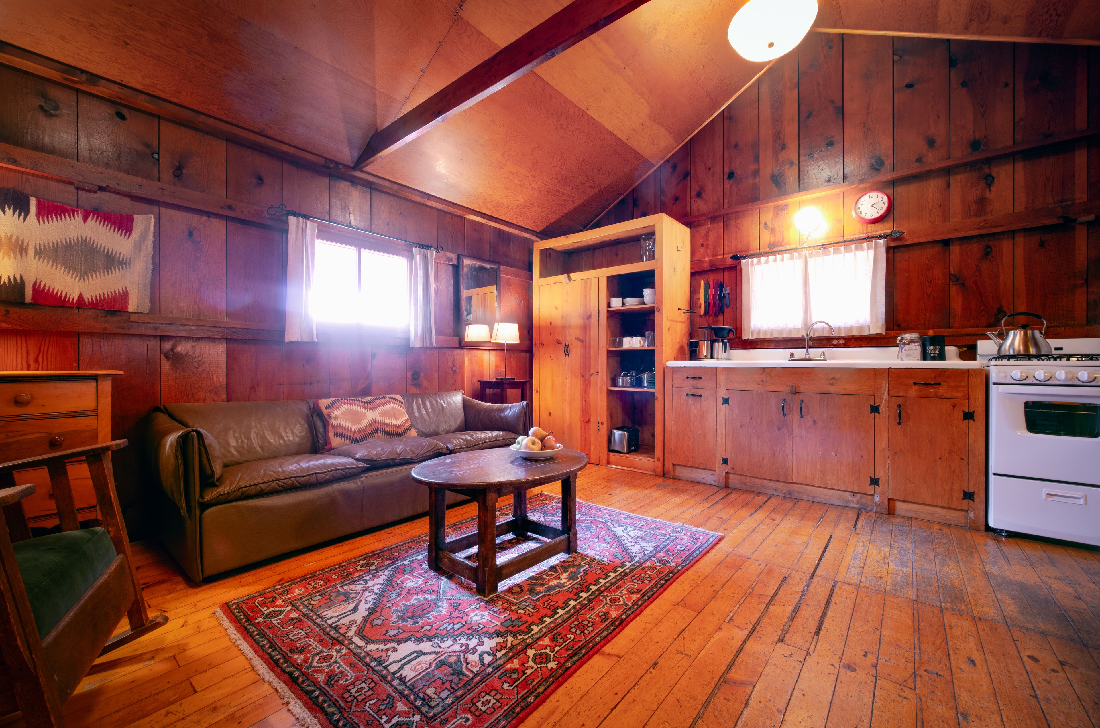Ein gemütliches Blockhaus-Interieur mit Holzbalkendecke, Ledersofa, Esstisch und Küchenzeile mit Holzausstattung und Herd.