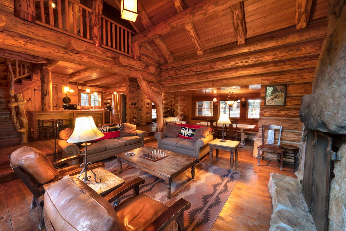 Interior rústico de cabaña con muebles de madera, chimenea y una zona de estar acogedora.
