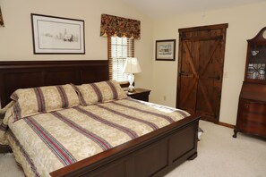 A bedroom with a large bed, a nightstand, a dresser, and a window with blinds.