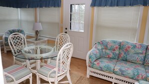 A living room with a glass-top table surrounded by white wicker chairs, a floral sofa, and a door with a window. - Peaceful 3BR 2.5 Bath Home Near Sparta NC & Blue Ridge Parkway Sleeps 6 (Glade Valley)