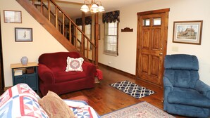 A living room with a wooden staircase, a red armchair, a blue recliner, and a patterned rug. - Peaceful 3BR 2.5 Bath Home Near Sparta NC & Blue Ridge Parkway Sleeps 6 (Glade Valley)