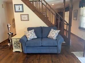 A blue sofa with floral cushions, a wooden floor, a staircase, and a wall-mounted picture frame. - Peaceful 3BR 2.5 Bath Home Near Sparta NC & Blue Ridge Parkway Sleeps 6 (Glade Valley)