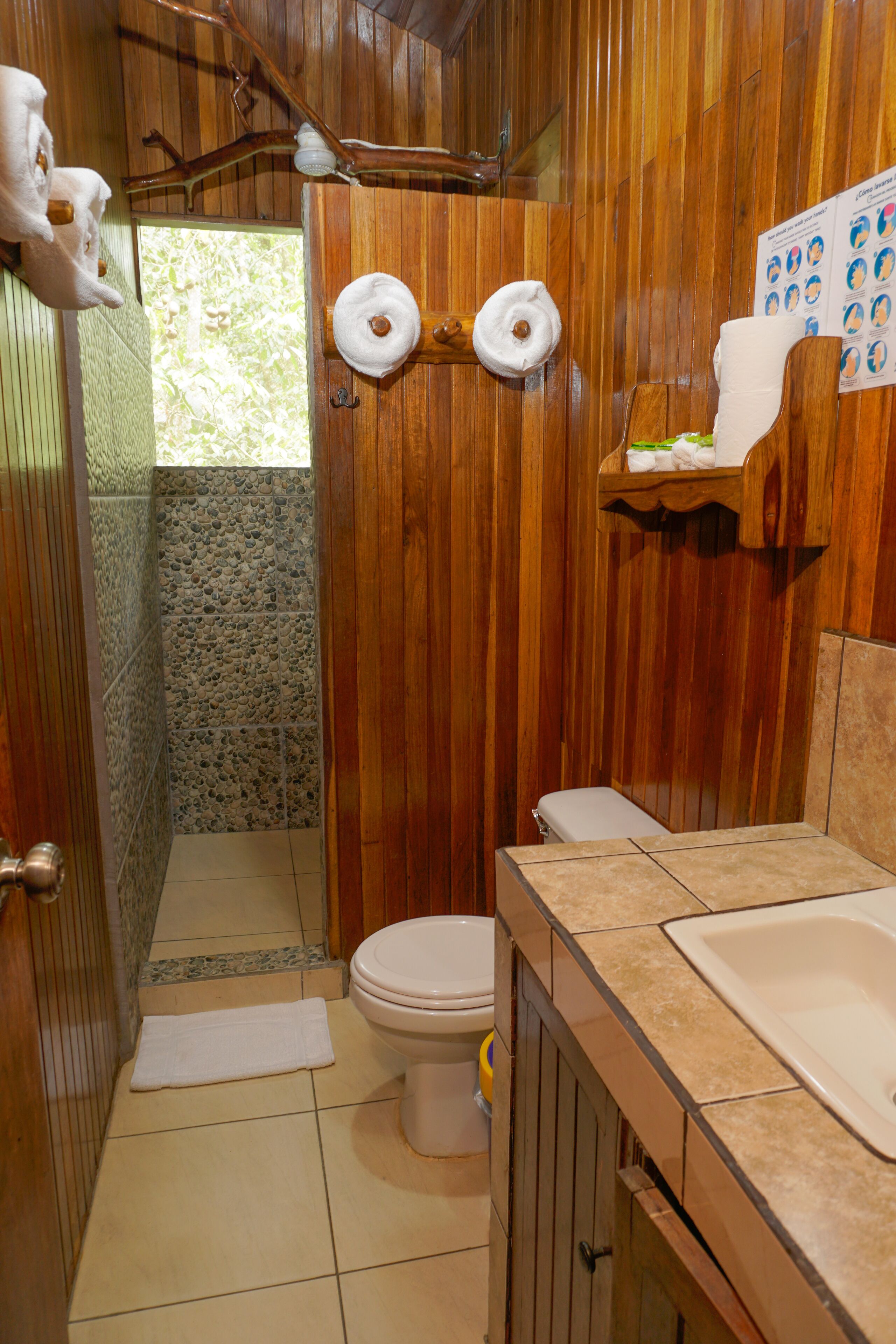 Une salle de bain avec des murs en bois, des toilettes, un lavabo et un espace douche.
