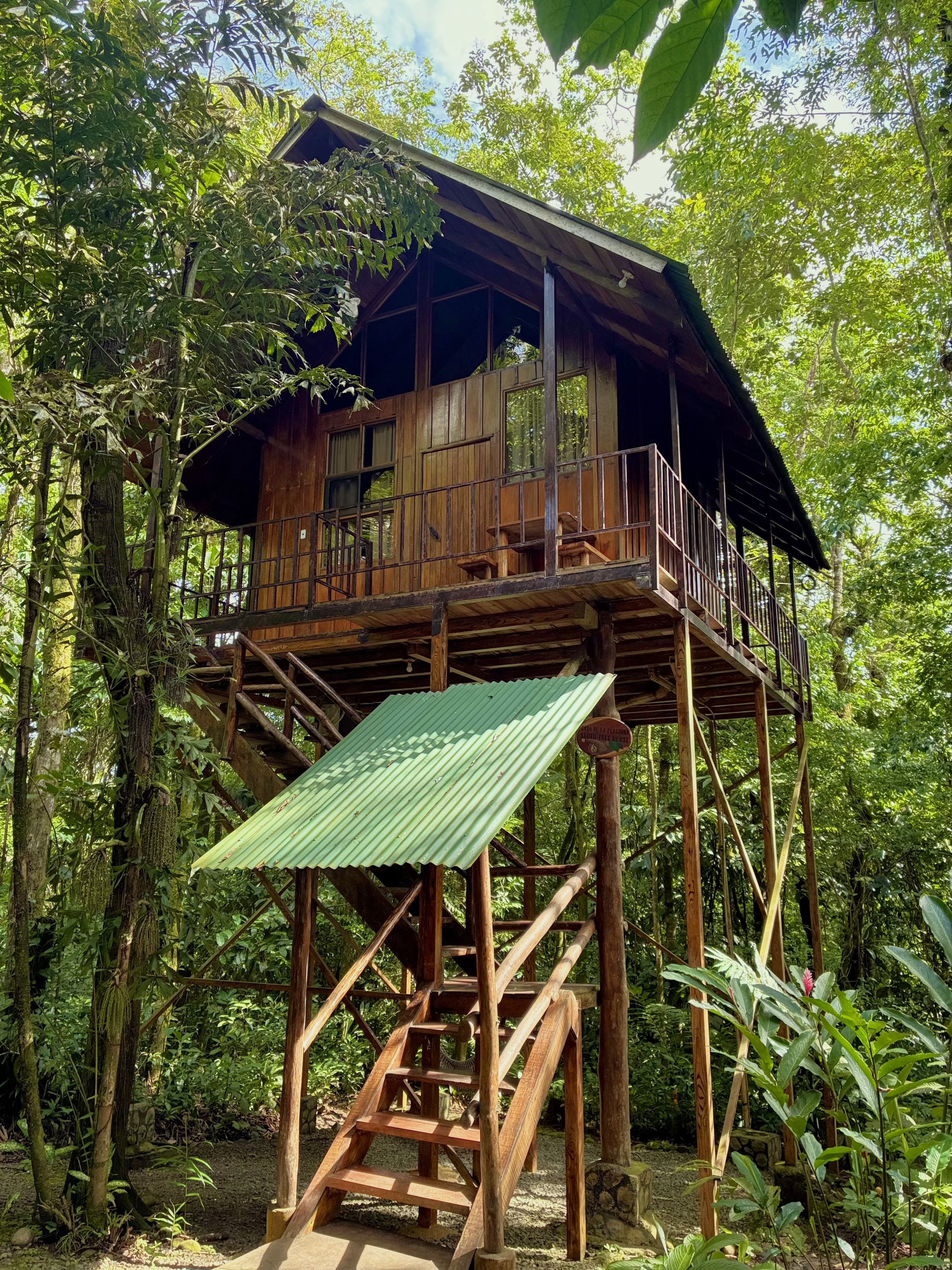 Una casa del árbol de madera con balcón y una escalera que lleva a ella.