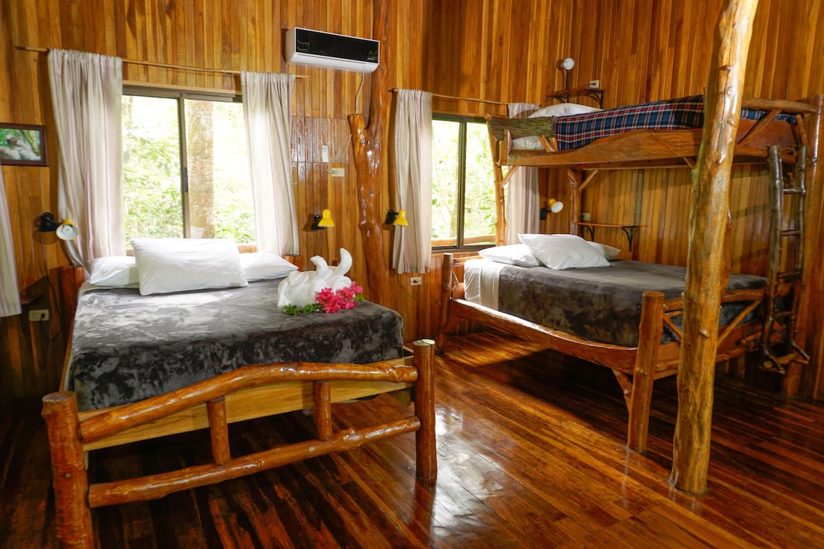 A wooden cabin with two bunk beds, a wooden floor, and a window with curtains.