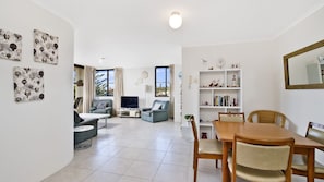 A modern living room with a television, seating area, and a dining table with chairs. - Sundial 503, Hollingworth Street (Port Macquarie)