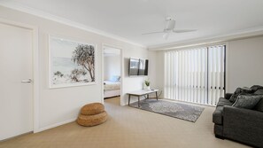 A living room with a sofa, a television, a ceiling fan, a door, and a framed picture on the wall.