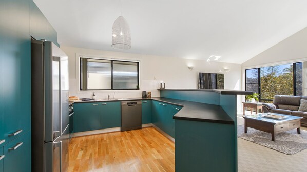 A modern kitchen with teal cabinetry, a dishwasher, and a large window.