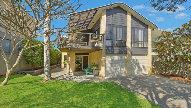 Ein zweistöckiges Haus mit überdachter Terrasse, Garage und gepflegtem Rasen.