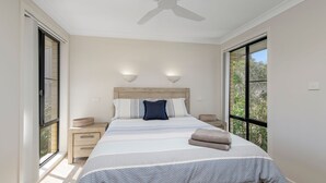 Ein Schlafzimmer mit einem großen Bett, zwei Nachttischen, einem Deckenventilator und Blick durch große Fenster.