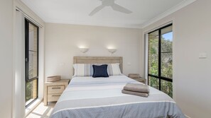 Una camera da letto con un letto grande, due comodini, una ventola a soffitto e vista panoramica da ampie finestre.