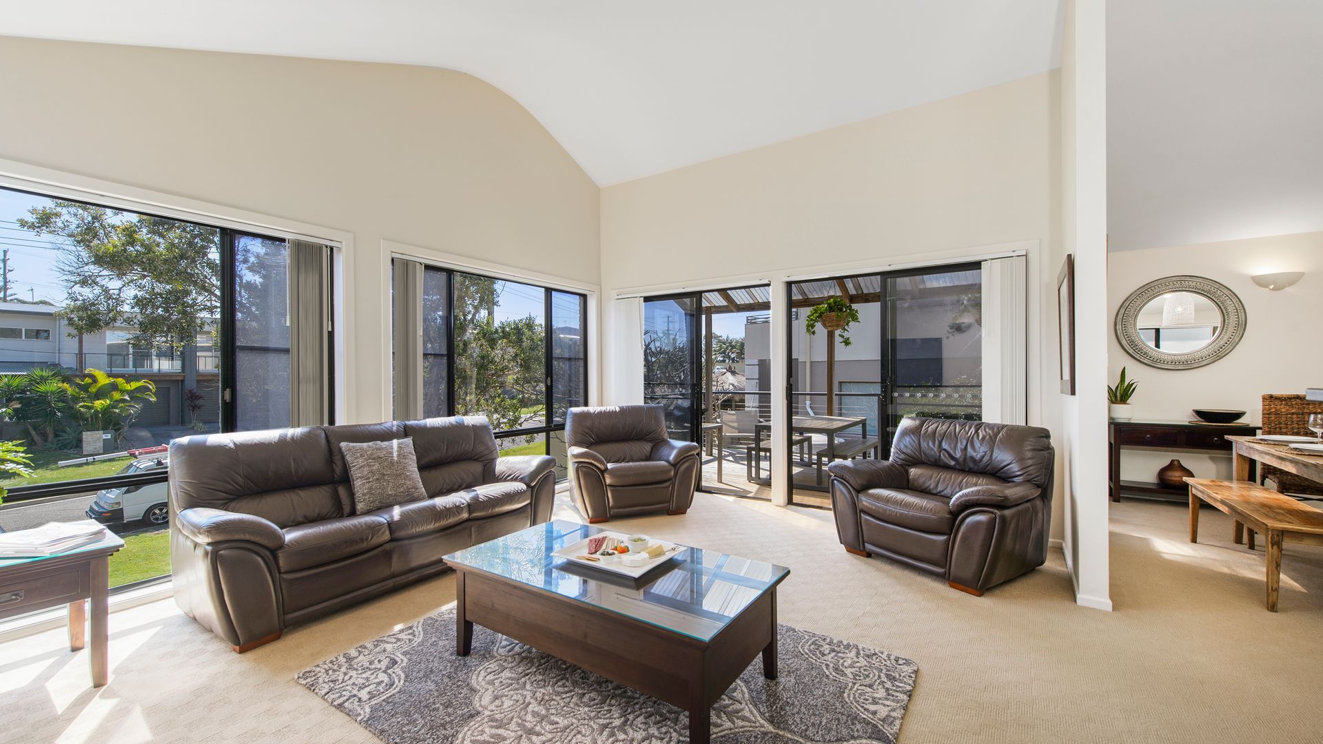 A modern living room with a glass coffee table, leather sofas, and a dining area with a wooden table and chairs.