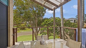 A balcony with a wooden railing, a table with a vase, and a view of a residential area with trees and houses.