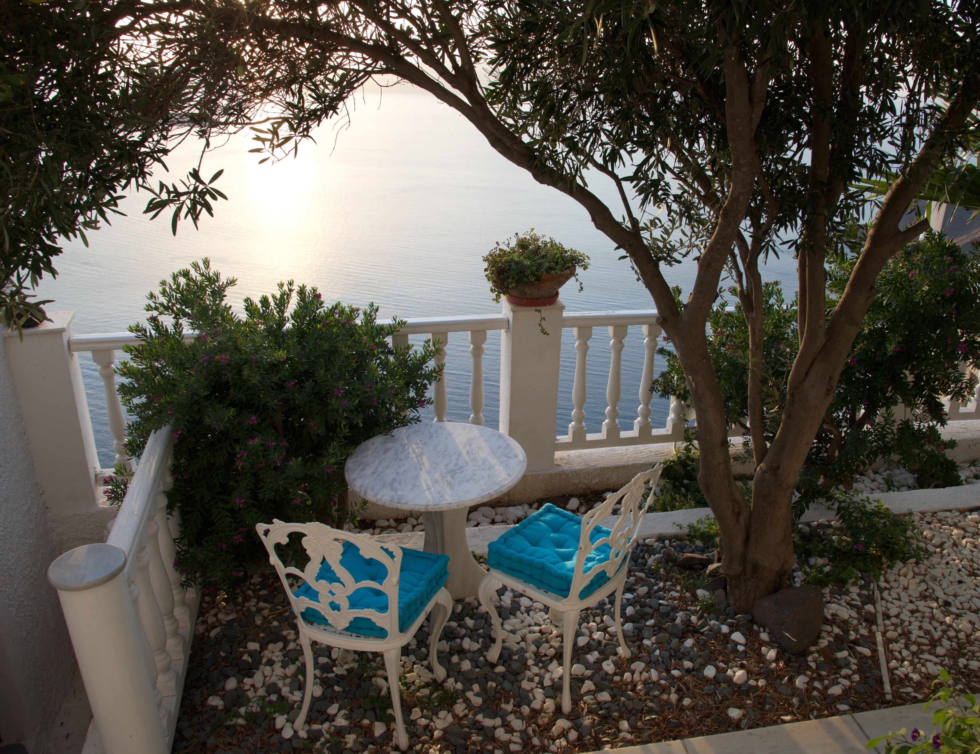 An outdoor seating area with a table and two chairs, surrounded by a white railing and a view of the sea.