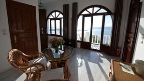 Ein Zimmer mit Esstisch, Korbstühlen, einer Blumenvase und großen Bogenfenstern mit Meerblick.