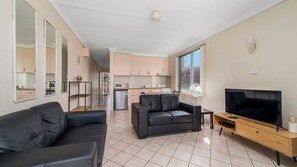 A modern living room with a sofa, a TV, and a kitchen in the background. - Ocean Court 7, 13 Lord Street (Port Macquarie)