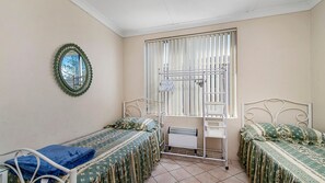 A bedroom with two single beds, a window with blinds, a radiator, and a mirror on the wall. - Ocean Court 7, 13 Lord Street (Port Macquarie)