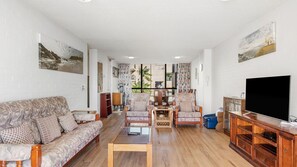 Una sala de estar con sofá, sillones, una mesa de centro, televisor y obras de arte en las paredes.