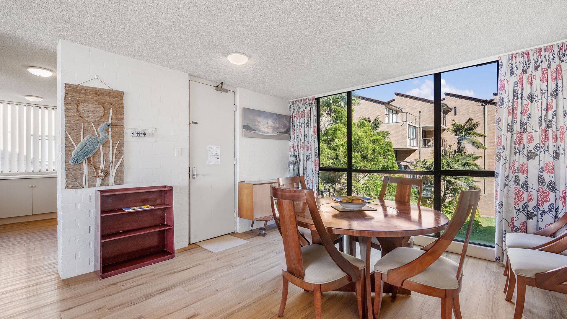 A dining area with a round table, chairs, and a view of a building through a window.