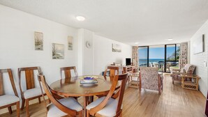 Een eethoek met een ronde tafel en stoelen, uitzicht op zee via een balkon, en kunstwerken aan de muur.