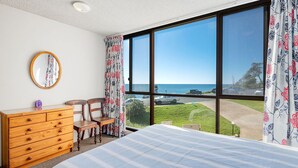 Een slaapkamer met een groot raam, een houten dressoir, een stoel en een bed.