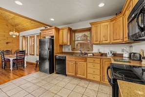 A kitchen with wooden cabinets, a black refrigerator, a dishwasher, a stove, and a dining area with a table and chairs.