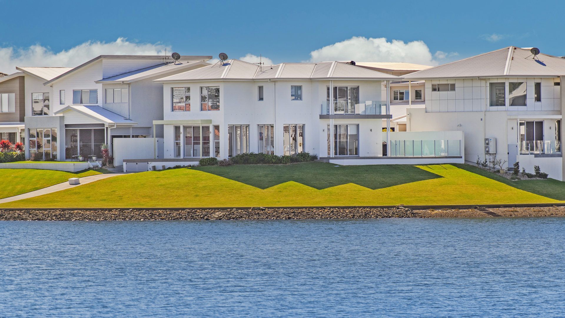 Een modern wooncomplex met meerdere huizen, een verzorgd gazon en een waterpartij op de voorgrond.