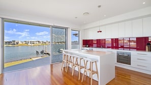 A modern kitchen with a large island, white cabinetry, and a view of a marina. - 4/84 The Anchorage, Port Macquarie (Port Macquarie)