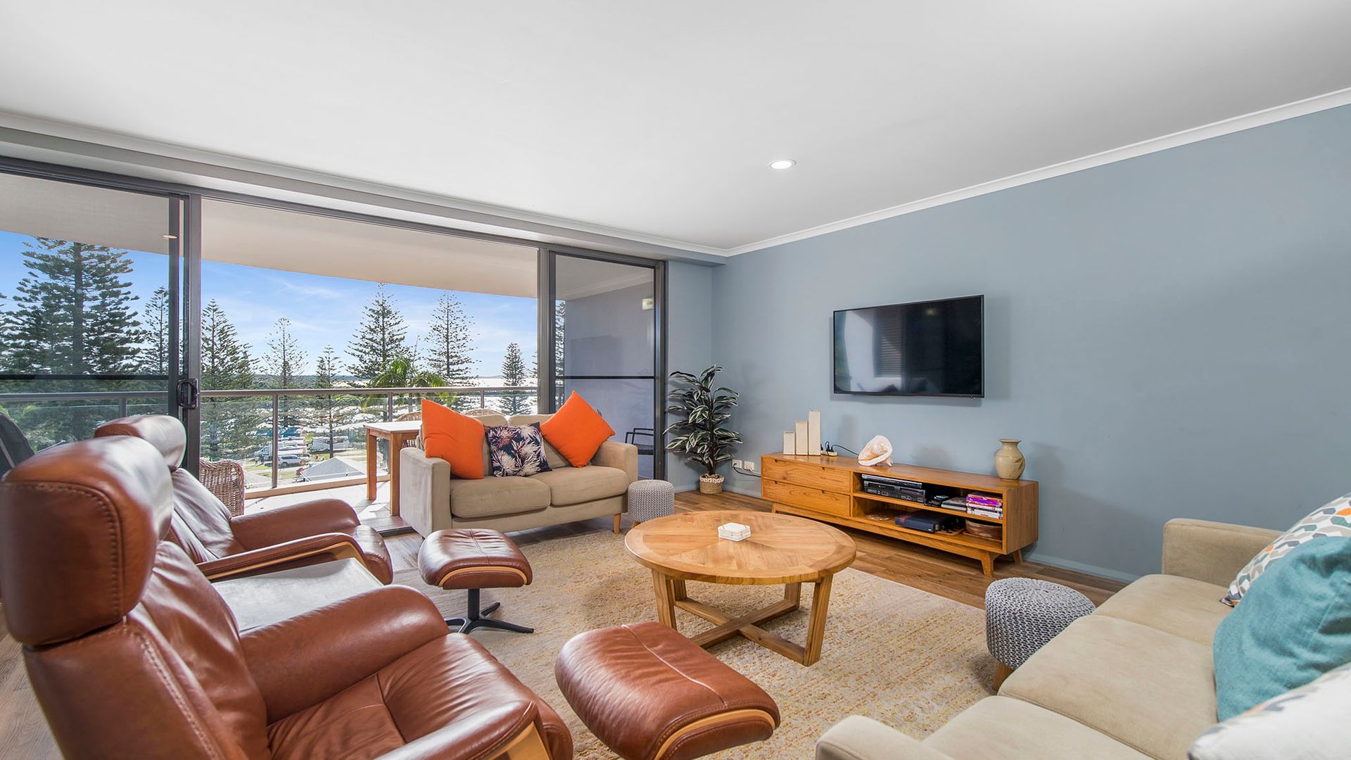 A modern living room with leather sofas, a coffee table, and a TV mounted on the wall.
