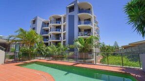A multi-story hotel with balconies, a swimming pool, and tropical landscaping.